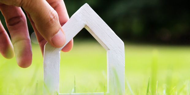 En hånd sætter model af lille hus i græsset. Foto: Colourbox.