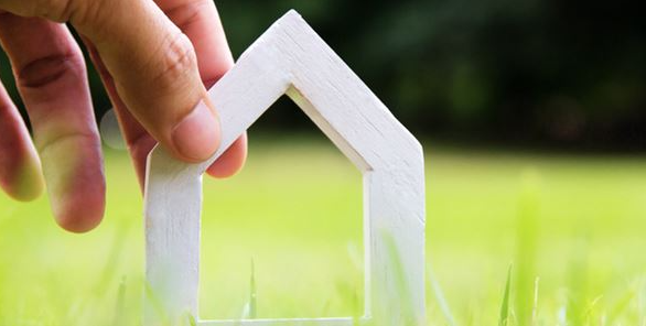 Hånd sætter lille hus i græsset. Foto: Colourbox.