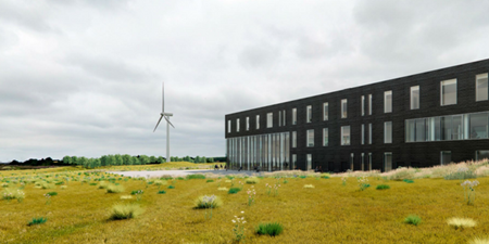 Erhvervsbygning med vindmølle i baggrunden. Visualisering: Foss